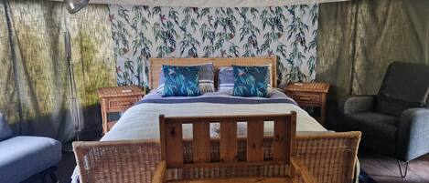 Une pièce aménagée avec une tente, un lit, deux chaises en bois, une table de chevet et une chaise.