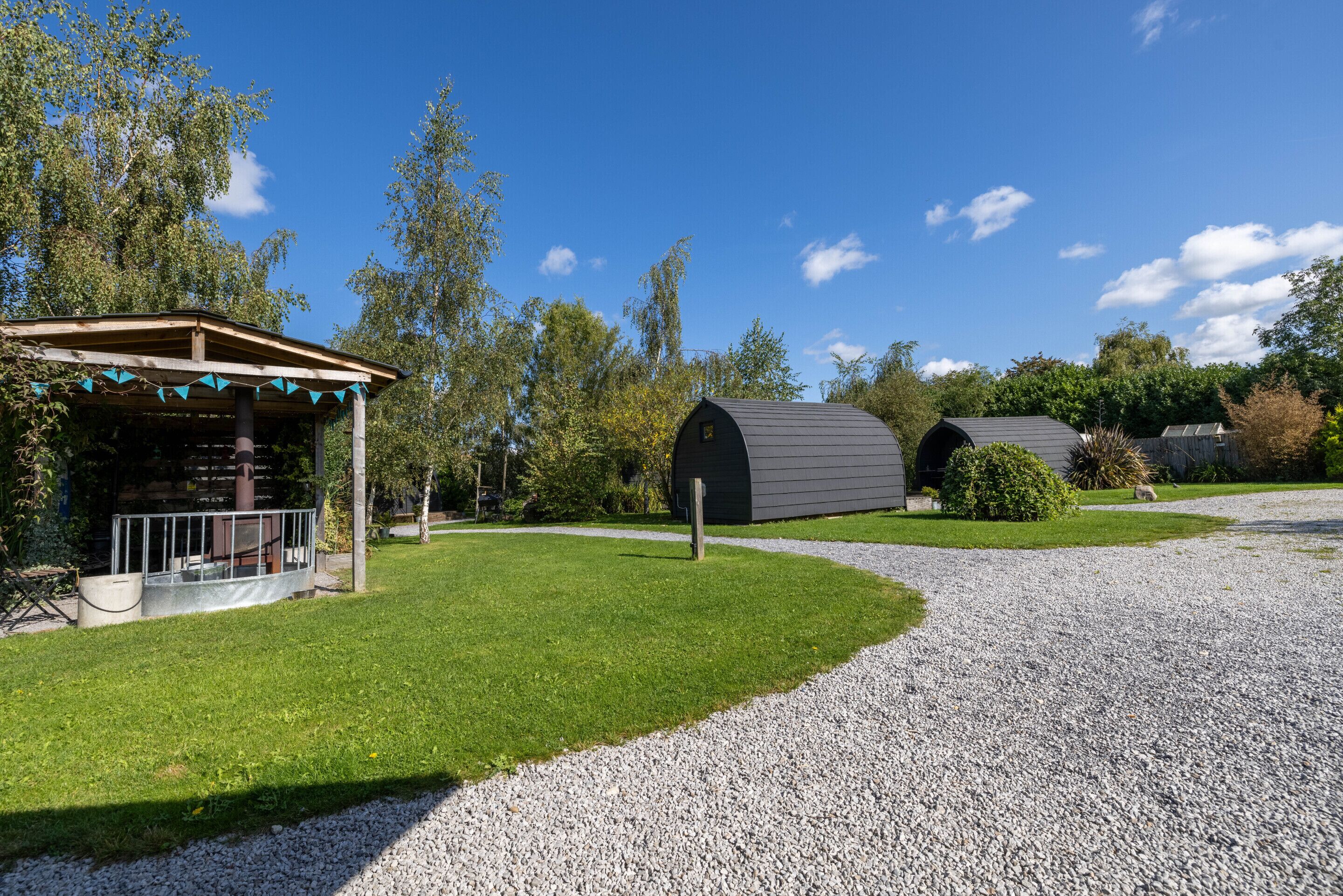 Un espacio al aire libre cubierto con una pérgola, un sendero de grava y un edificio con techo oscuro.