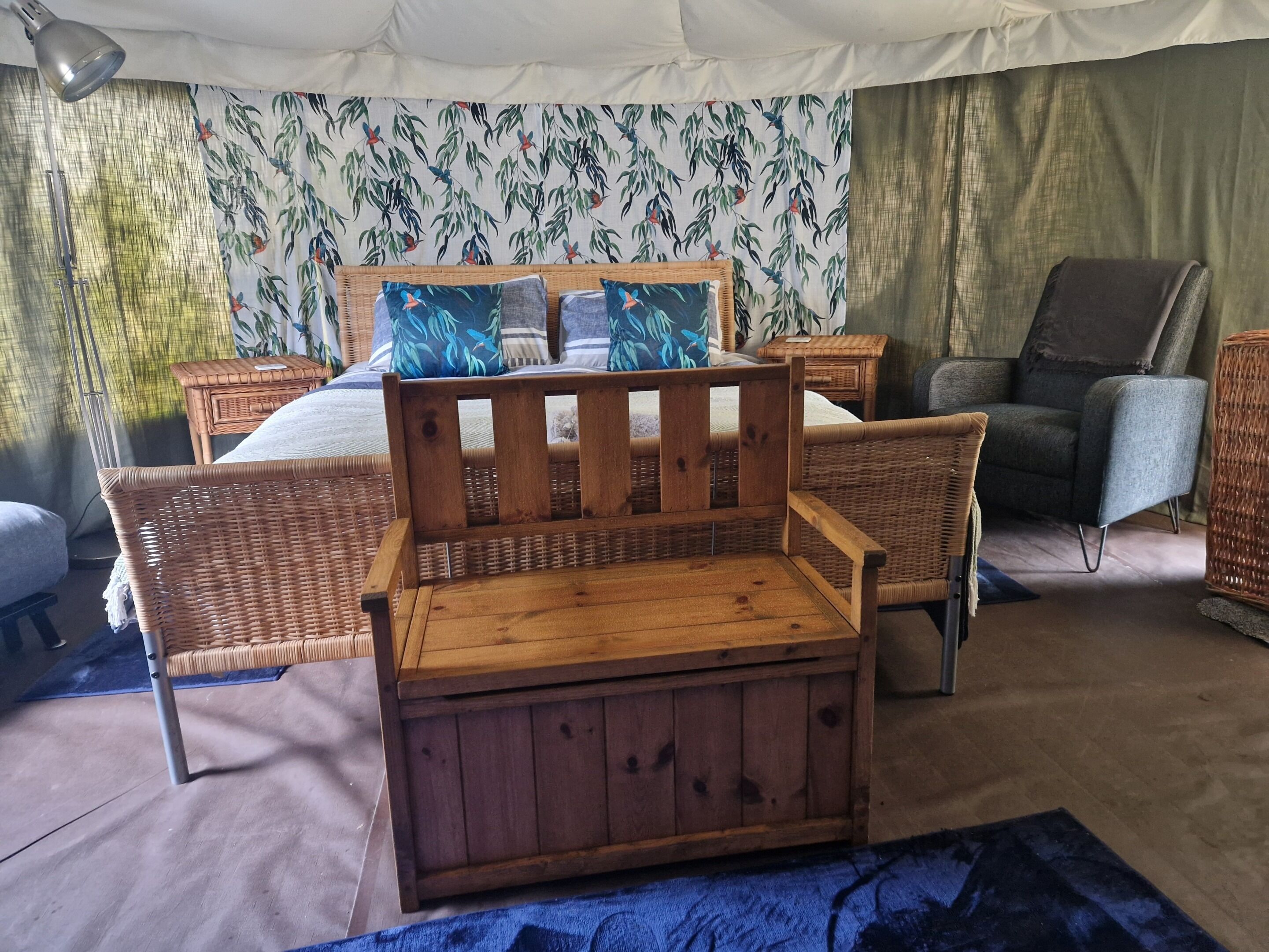A cozy room with a bed, two wicker chairs, a small wooden chest, and a grey armchair.
