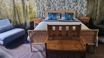 A cozy room with a bed, two wicker chairs, a small table, and a bench.
