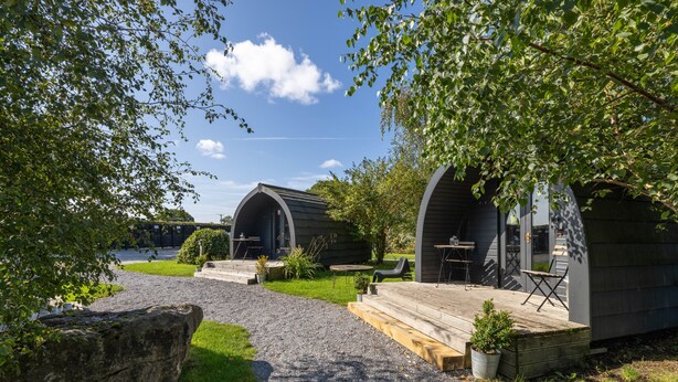 A campsite with two cabins, each with a wooden deck and outdoor seating. - The Little Hide - Adult Only Camping Pods (York)
