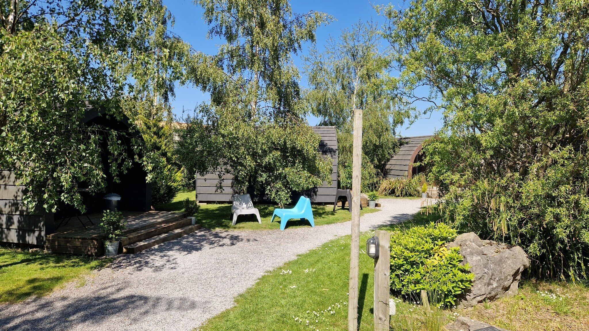 A garden area with a gravel path, a wooden bench, and a blue plastic chair.