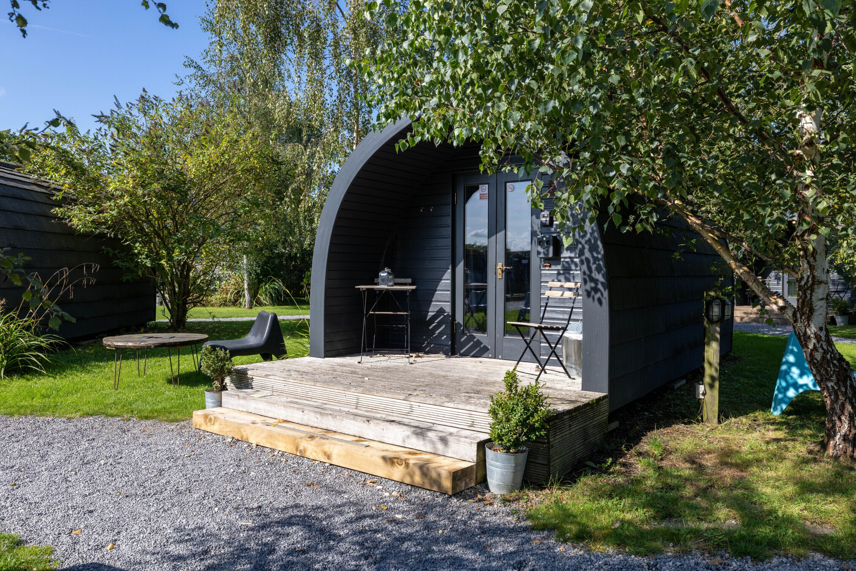 Eine moderne, halboffene Konstruktion mit Holzterrasse, Sitzgelegenheit im Freien und einem kleinen Tisch.