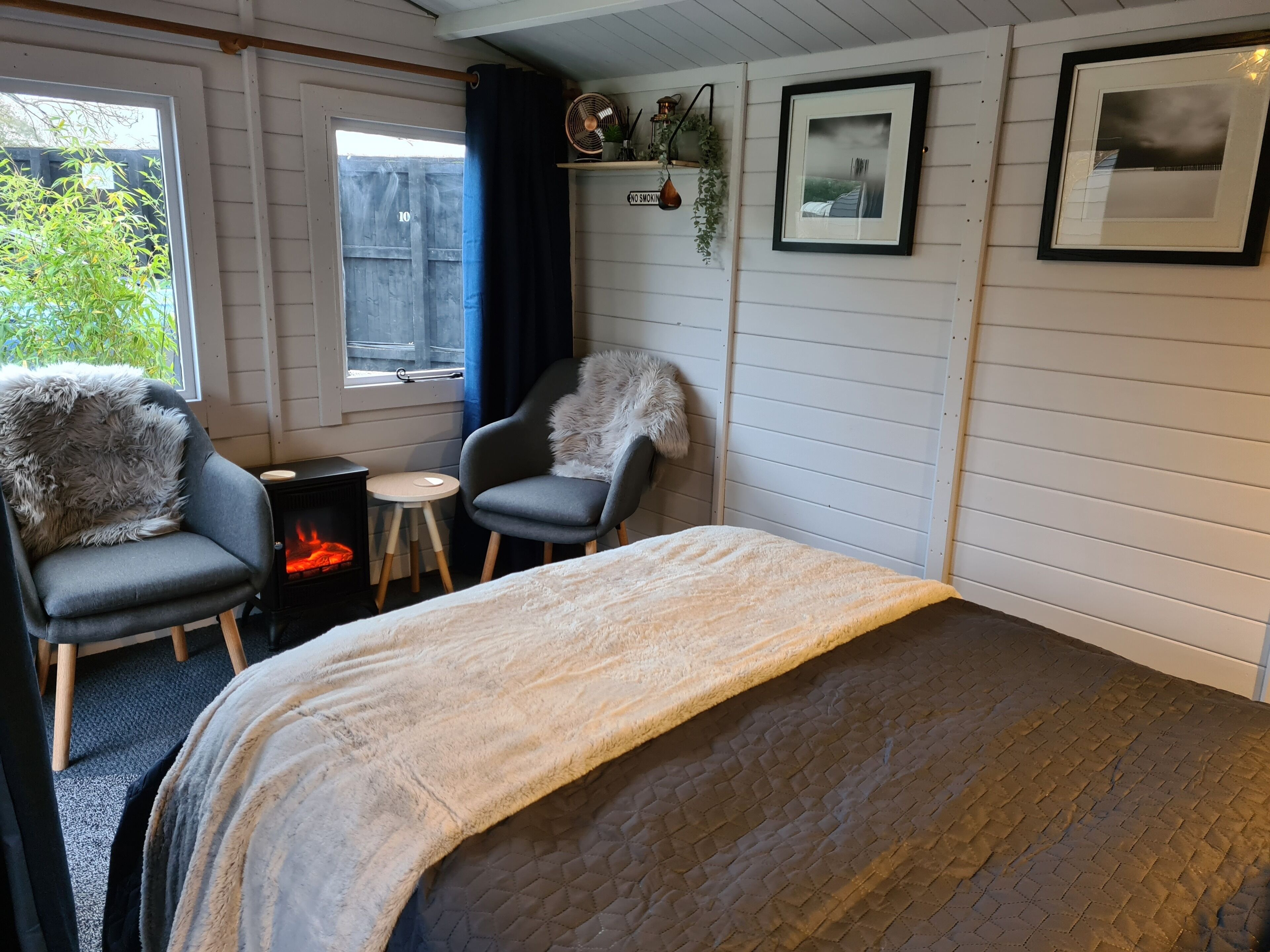 Une pièce confortable avec un lit, deux fauteuils, une petite table, une cheminée et une fenêtre donnant sur un paysage verdoyant.