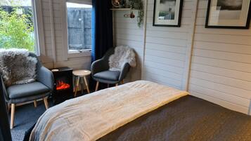 Une pièce confortable avec un lit, deux fauteuils, une petite table, une cheminée et une fenêtre donnant sur un paysage verdoyant.