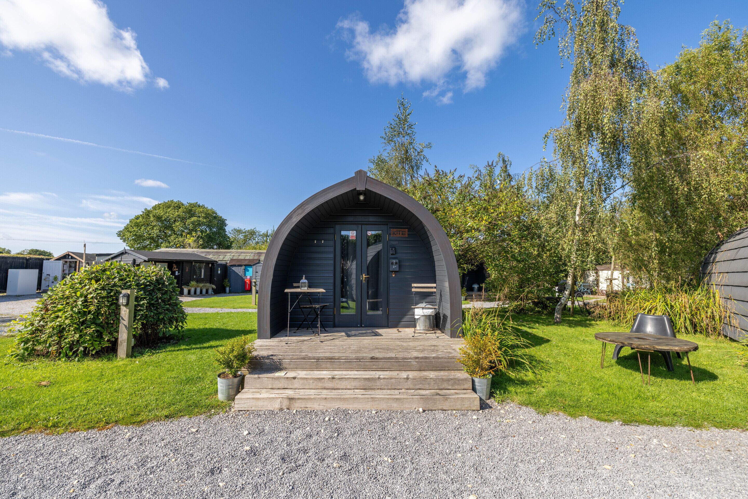 Un petit bâtiment aux couleurs sombres, doté d’une arche, avec une allée de gravier menant à une porte en bois.