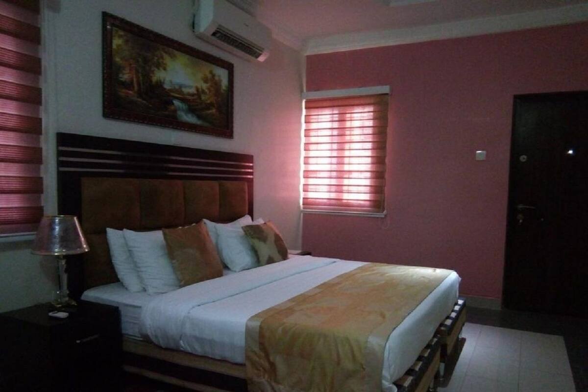 A bedroom with a bed, a nightstand, a lamp, a painting on the wall, and a window with blinds.