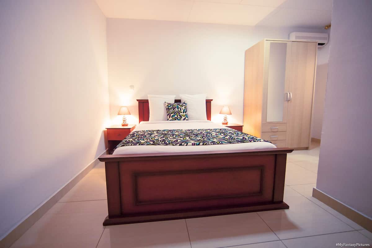 A bedroom with a bed, bedside lamps, a wardrobe, and a nightstand.
