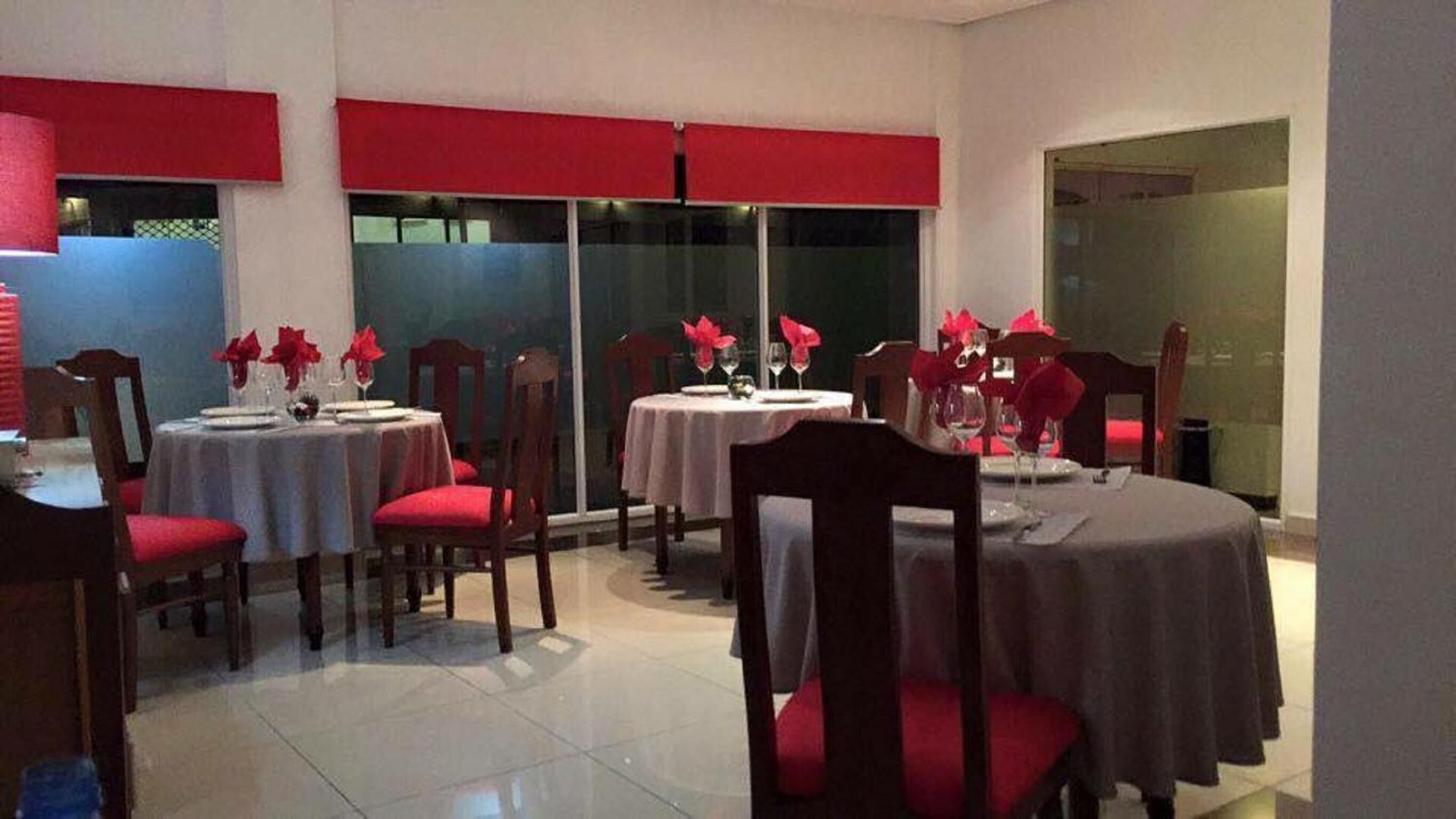 A dining area with round tables, red chairs, and white tablecloths.