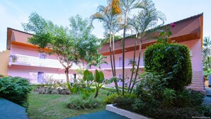 Un edificio de varios pisos con balcones, rodeado de abundante vegetación y palmeras.