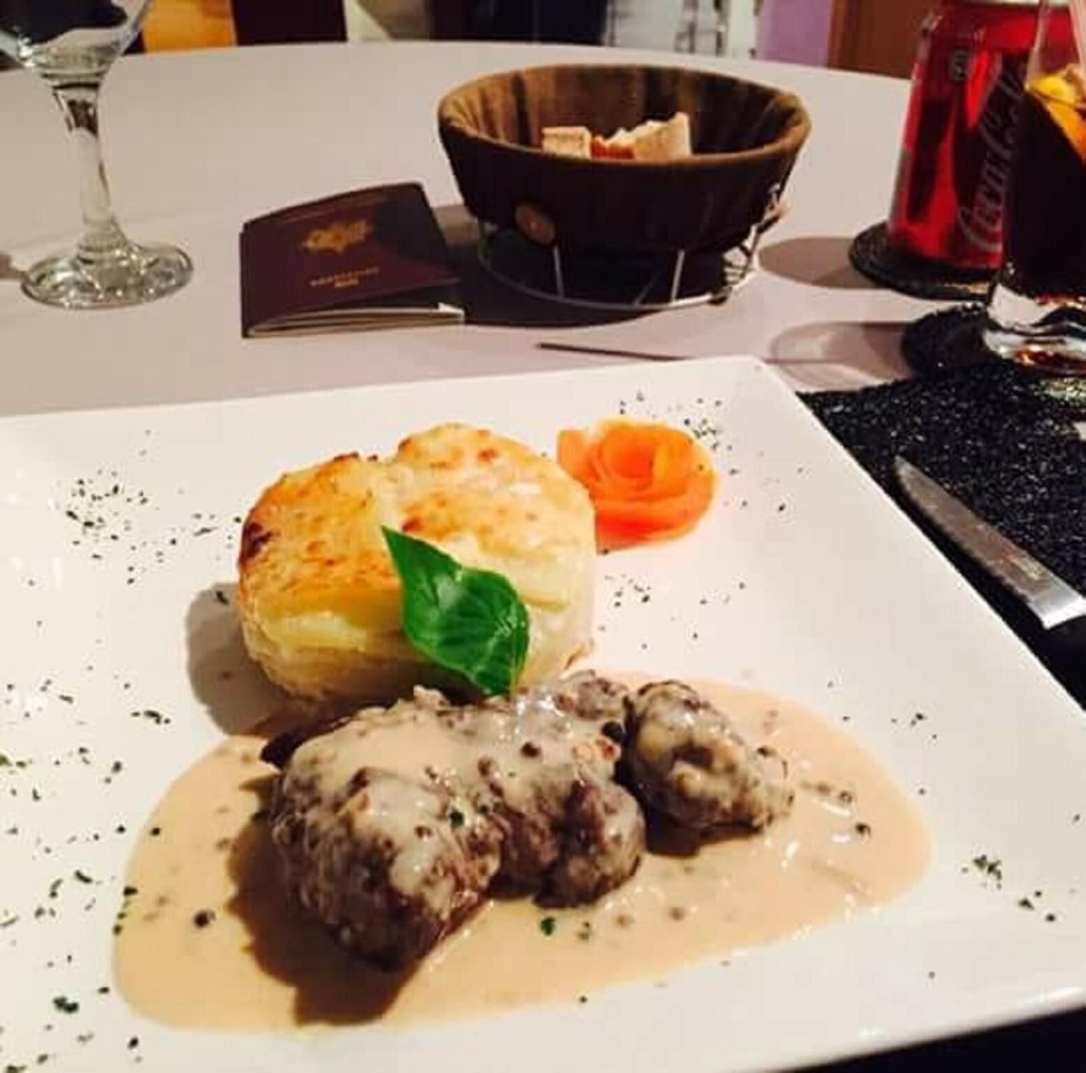 Un plato con albóndigas en salsa, una patata al horno y una zanahoria como decoración.