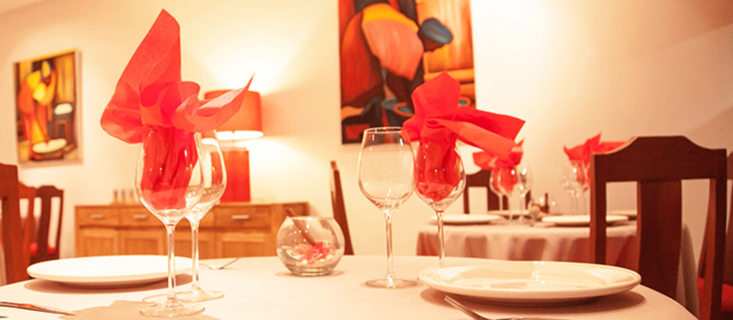 Une table à manger dressée avec des verres à vin et des assiettes, décorée de rubans rouges.