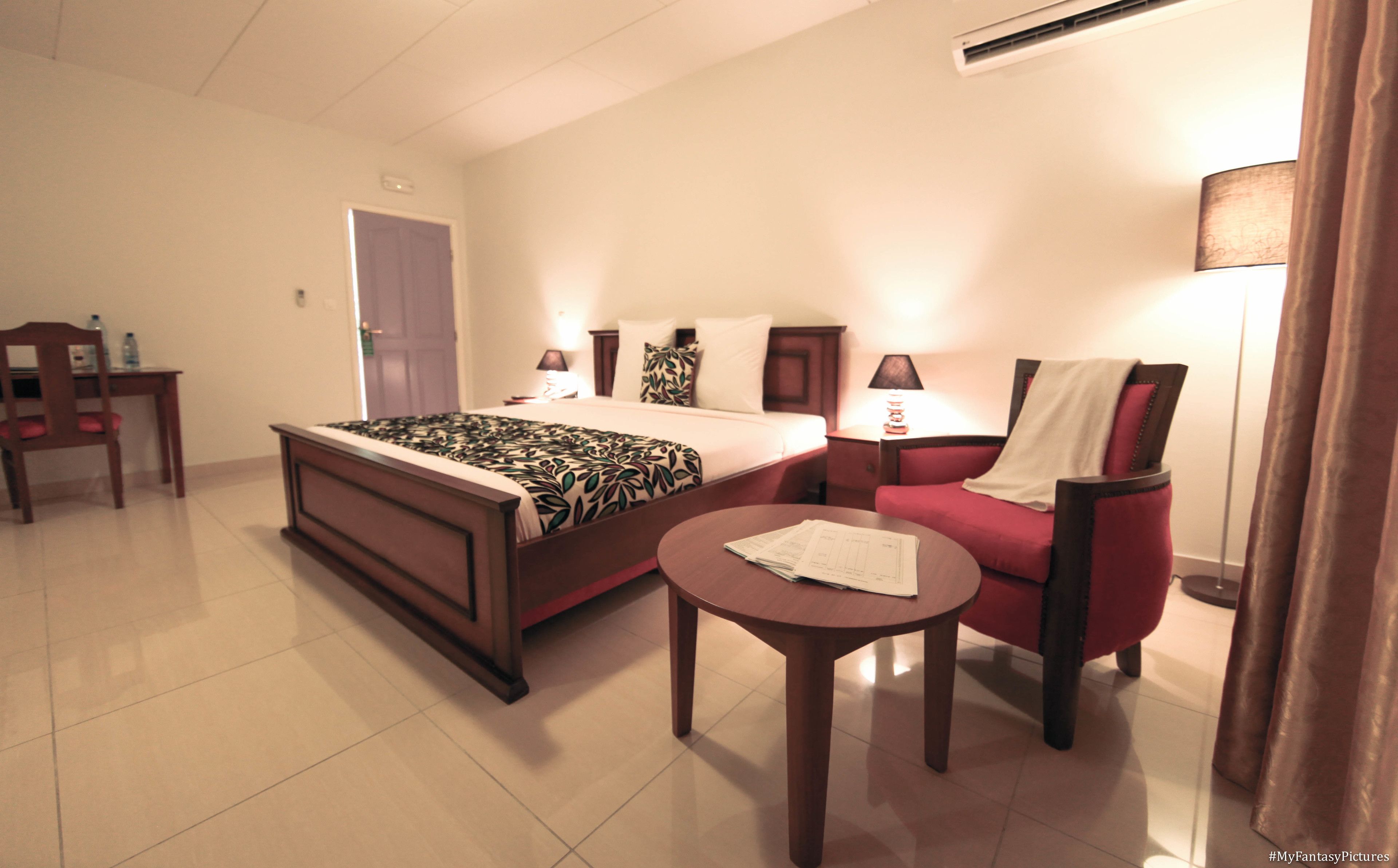 Habitación de hotel con cama, escritorio, silla, mesa redonda y lámpara.