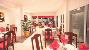 Comedor con mesas redondas, sillas rojas y plantas en macetas.