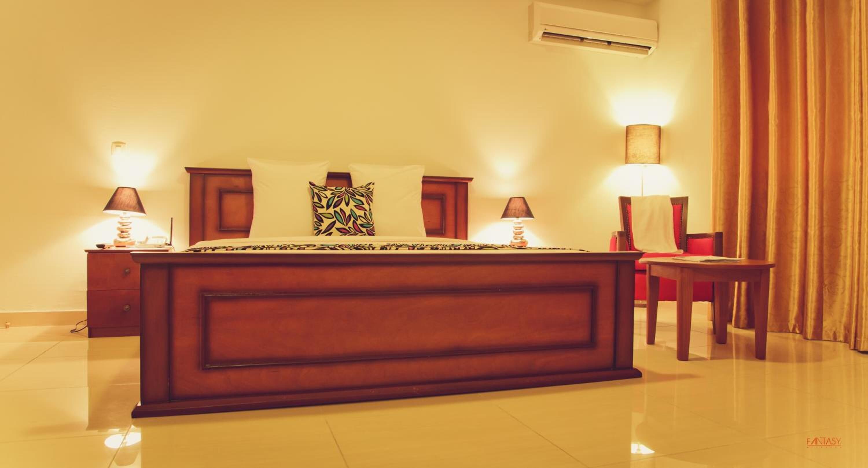 A hotel room with a large bed, two bedside tables, a nightstand, a lamp, and a curtain.