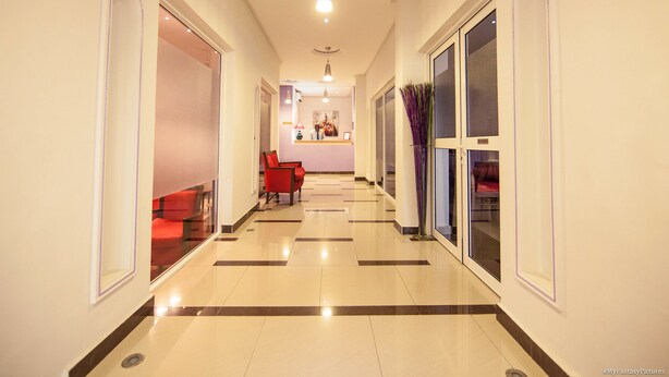 Un pasillo de hotel con una silla roja, una recepción y un florero con flores moradas.