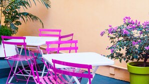Un comedor con sillas rosas y una mesa blanca, un cuadro de cebra en la pared y una planta en maceta con flores púrpuras.
