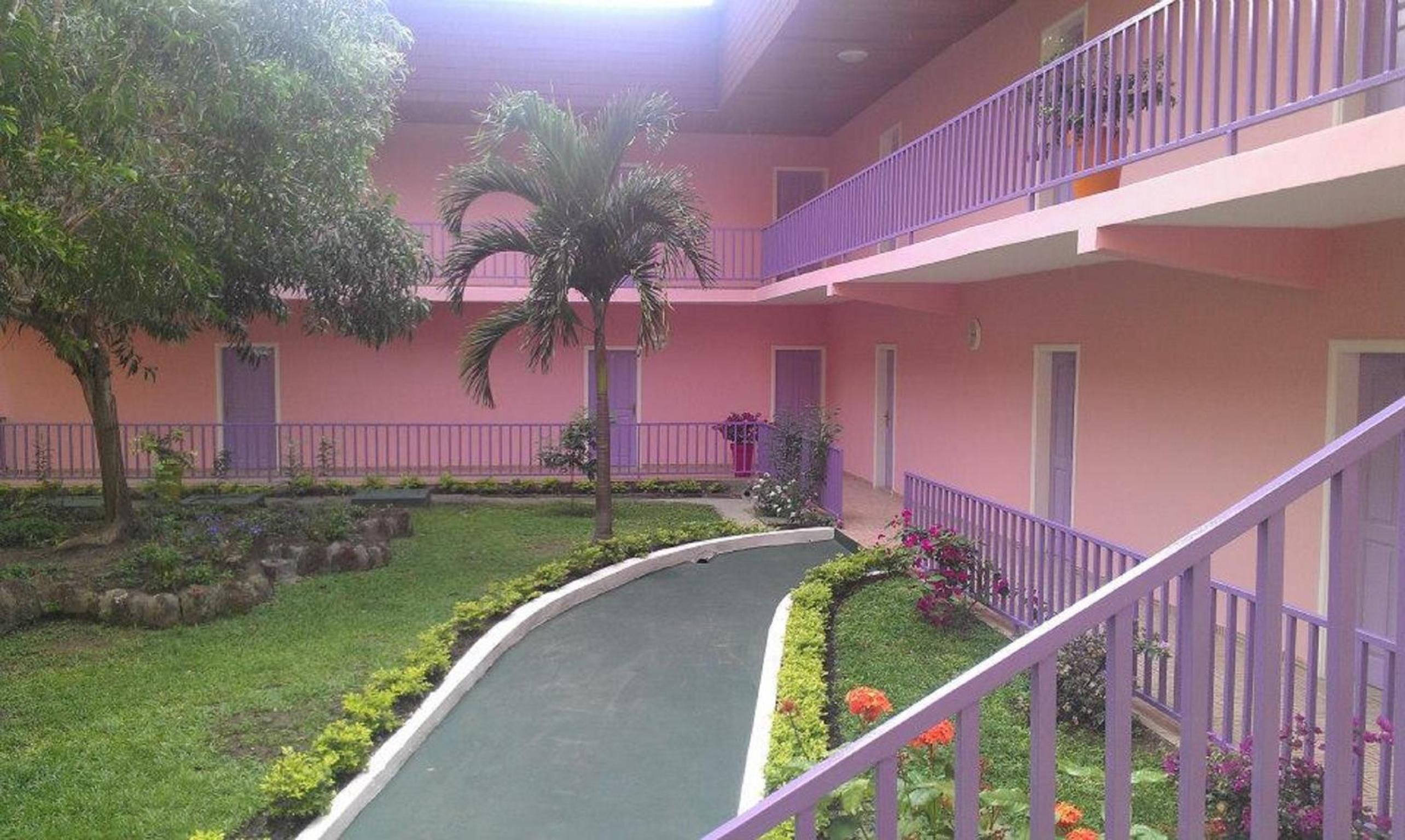 A multi-level building with a curved pathway, surrounded by greenery and a purple railing.