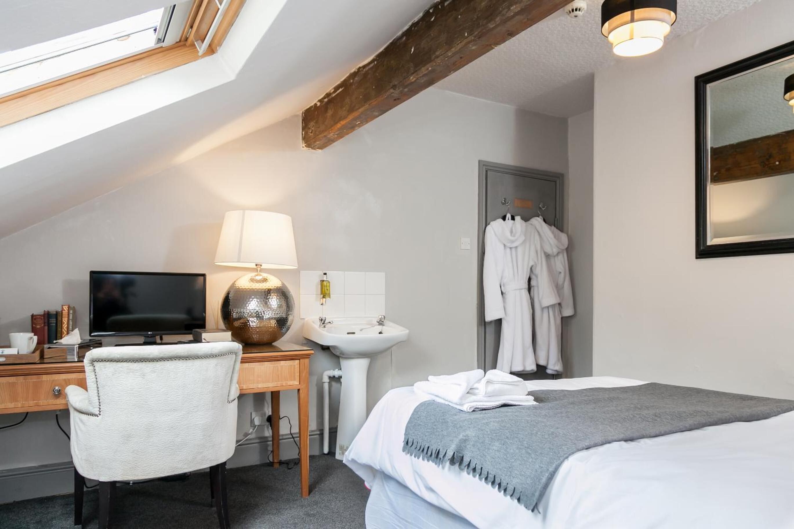 Een hotelkamer met een bureau, een televisie, een lamp, een wastafel, een bed en een spiegel.