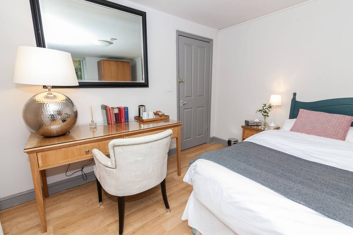 Une chambre bien rangée, avec un lit, un bureau doté d’une lampe, une chaise et un miroir.