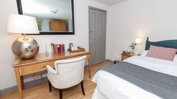Un dormitorio ordenado con cama, escritorio con lámpara, silla y espejo.