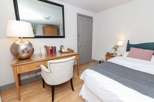Un dormitorio ordenado con cama, escritorio con lámpara, silla y espejo.