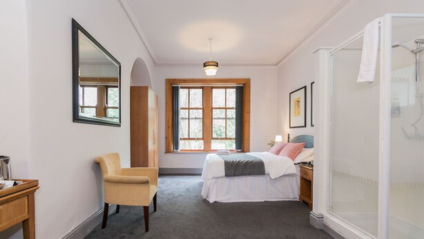 Un dormitorio con cama, una silla, un escritorio, una ventana y ducha.