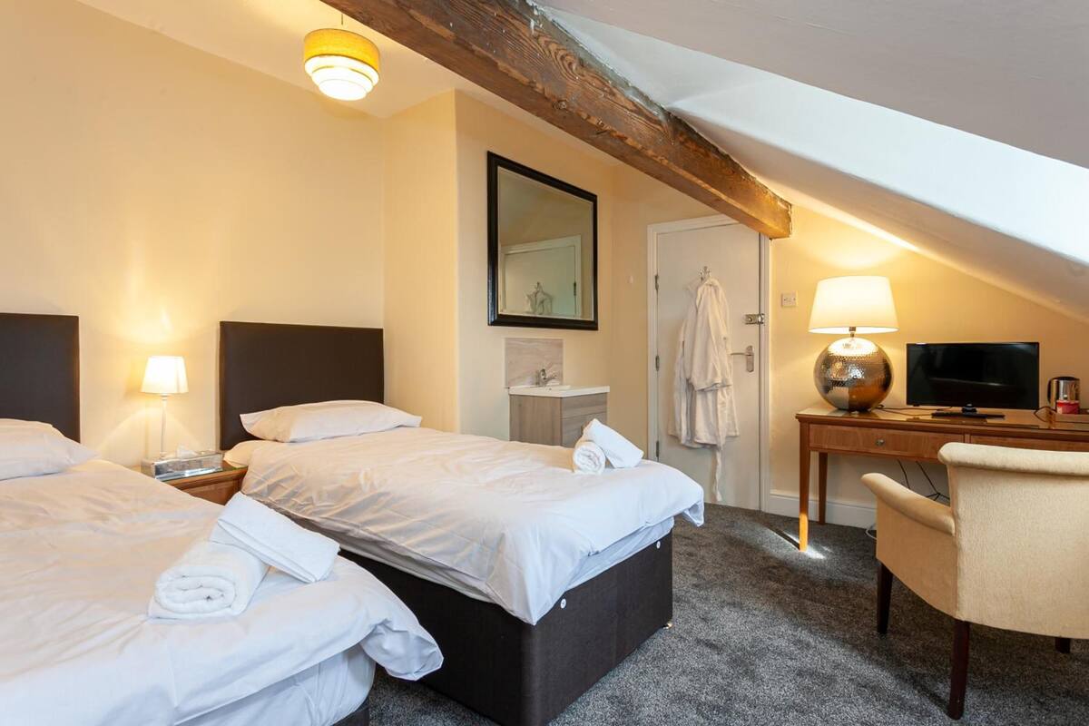 Une chambre d’hôtel avec deux lits, un bureau avec une télévision, un miroir et une lampe.