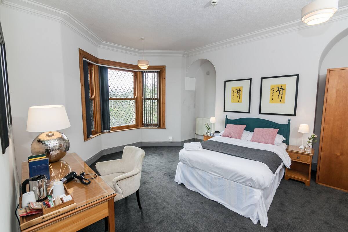 Une chambre bien rangée, avec un lit, des tables de chevet, une chaise, un bureau et une fenêtre avec des rideaux.