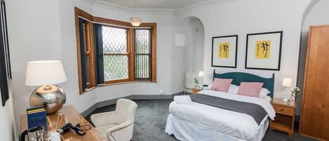 A neatly arranged bedroom with a bed, bedside tables, a chair, a desk, and a window with curtains.