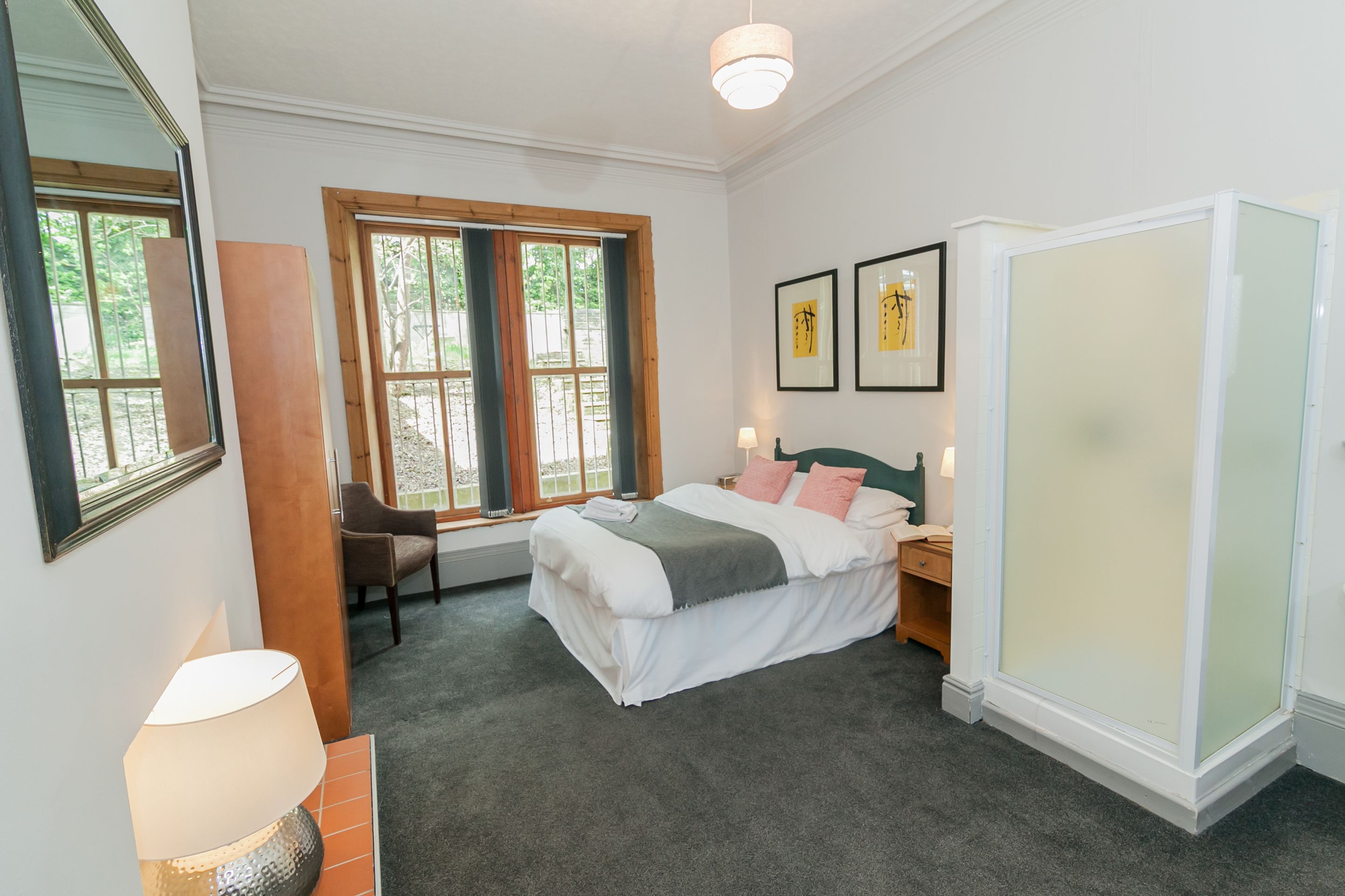 A bedroom with a bed, a desk, a chair, a lamp, and two framed pictures on the wall.