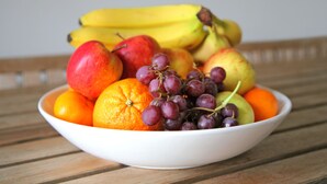 Un cuenco con fruta variada, incluyendo manzanas, naranjas, uvas y plátanos.