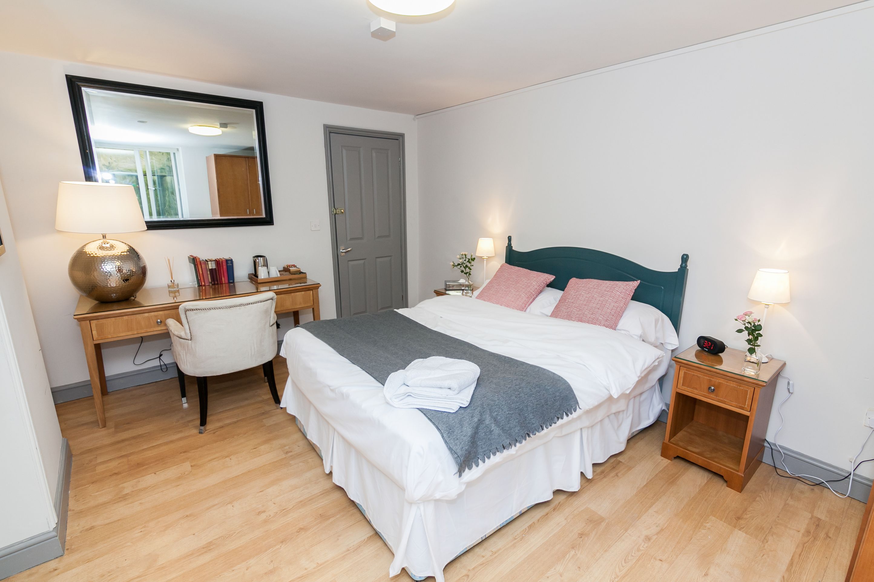 A neatly arranged bedroom with a bed, bedside tables, a desk, and a chair.