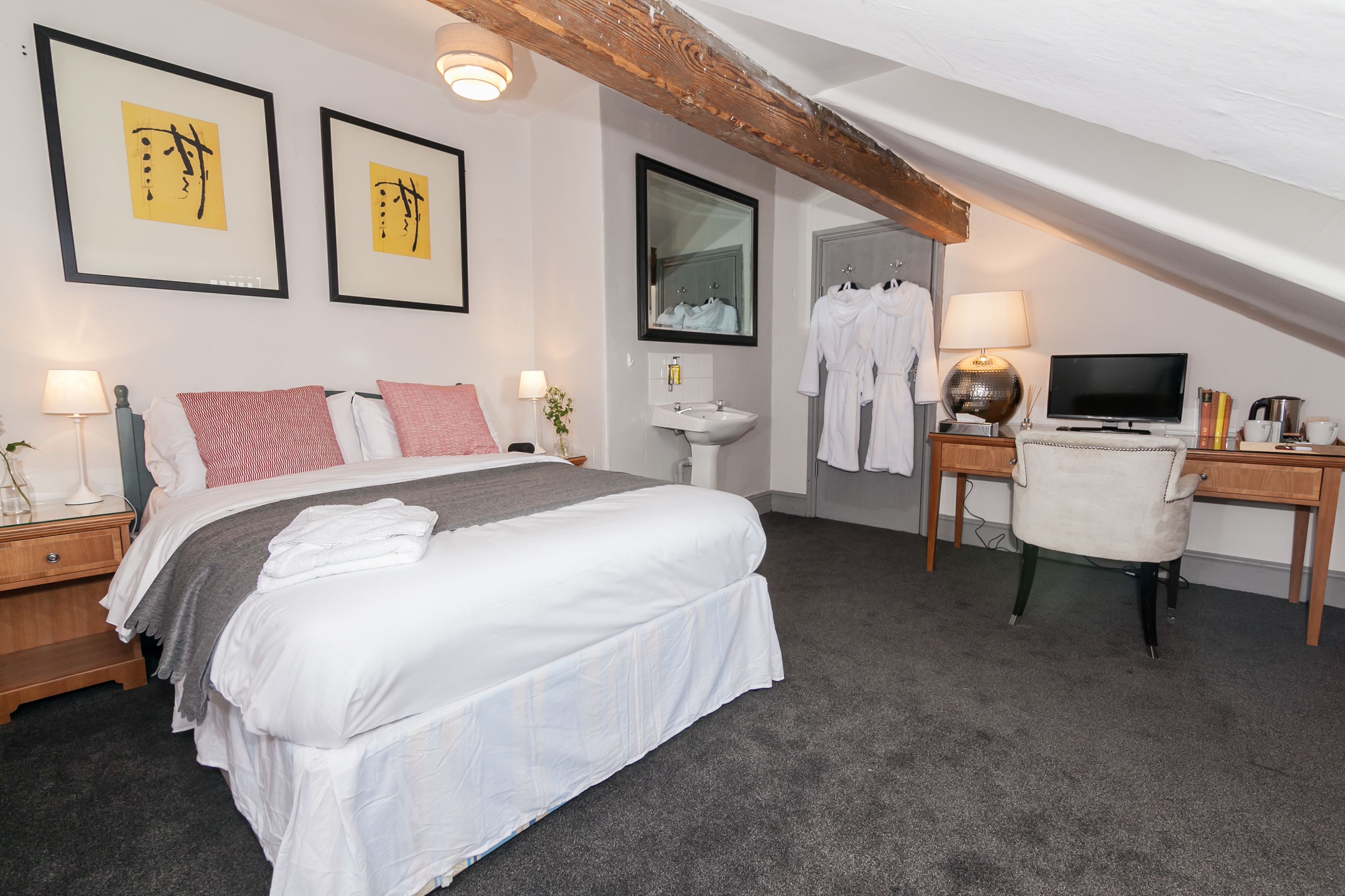 Une chambre à coucher avec un grand lit, des tables de chevet, un bureau, une chaise, une télévision, un miroir et des œuvres d’art accrochées au mur.