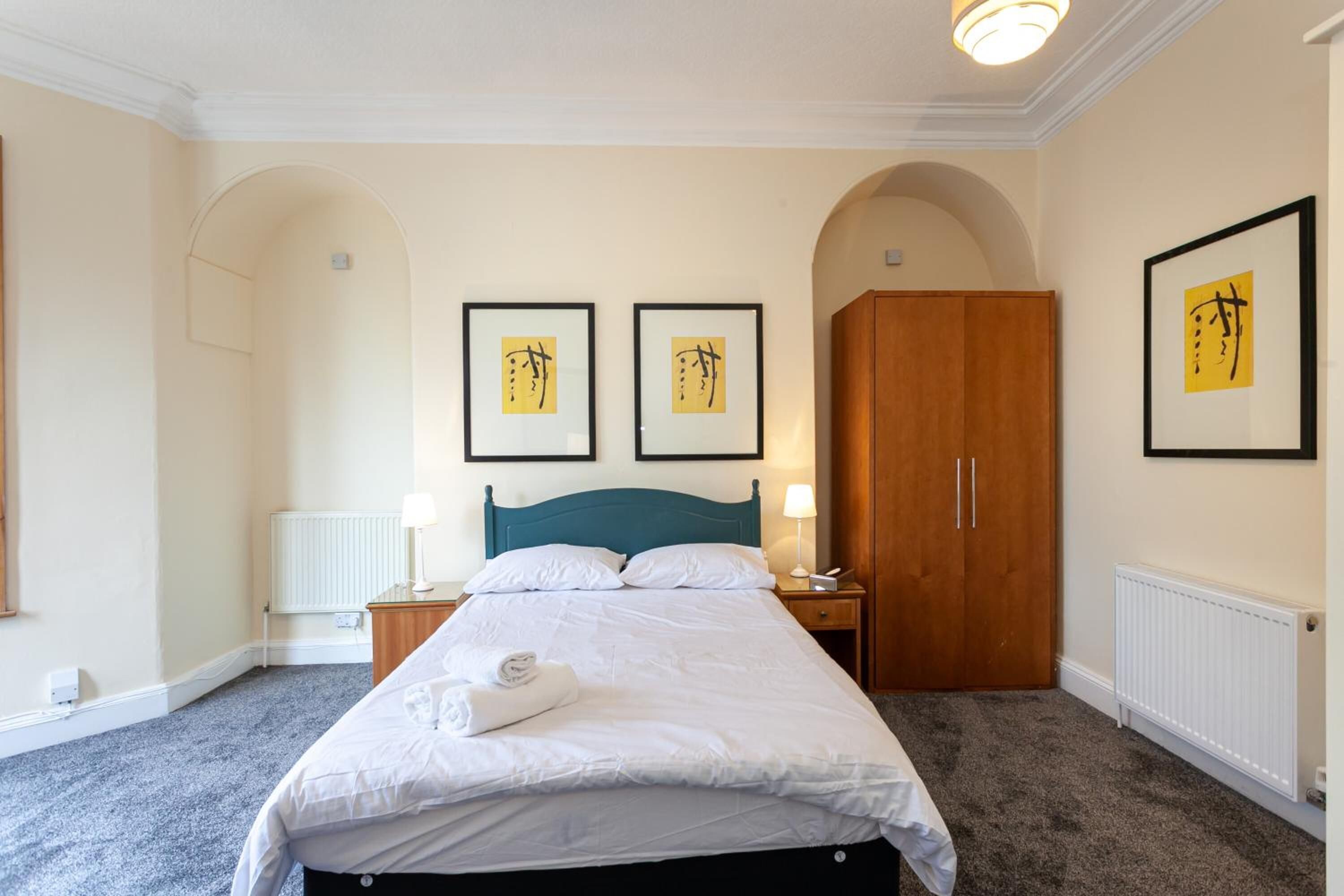 A neatly arranged bedroom with a bed, two bedside tables, a wardrobe, and framed artwork on the walls.