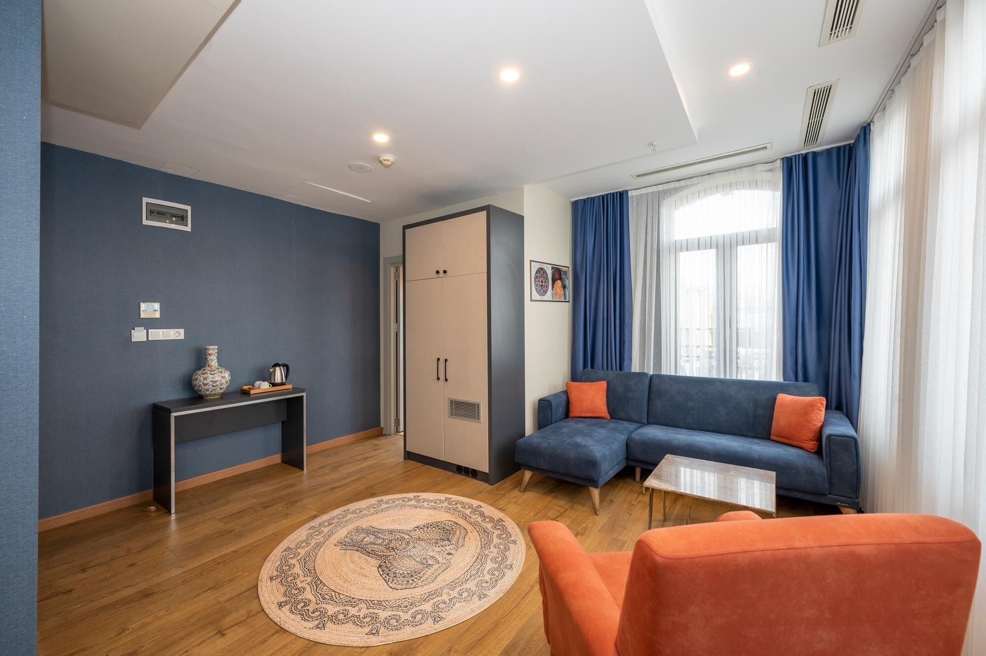 A modern living room with a blue sofa, orange armchair, and a round rug.