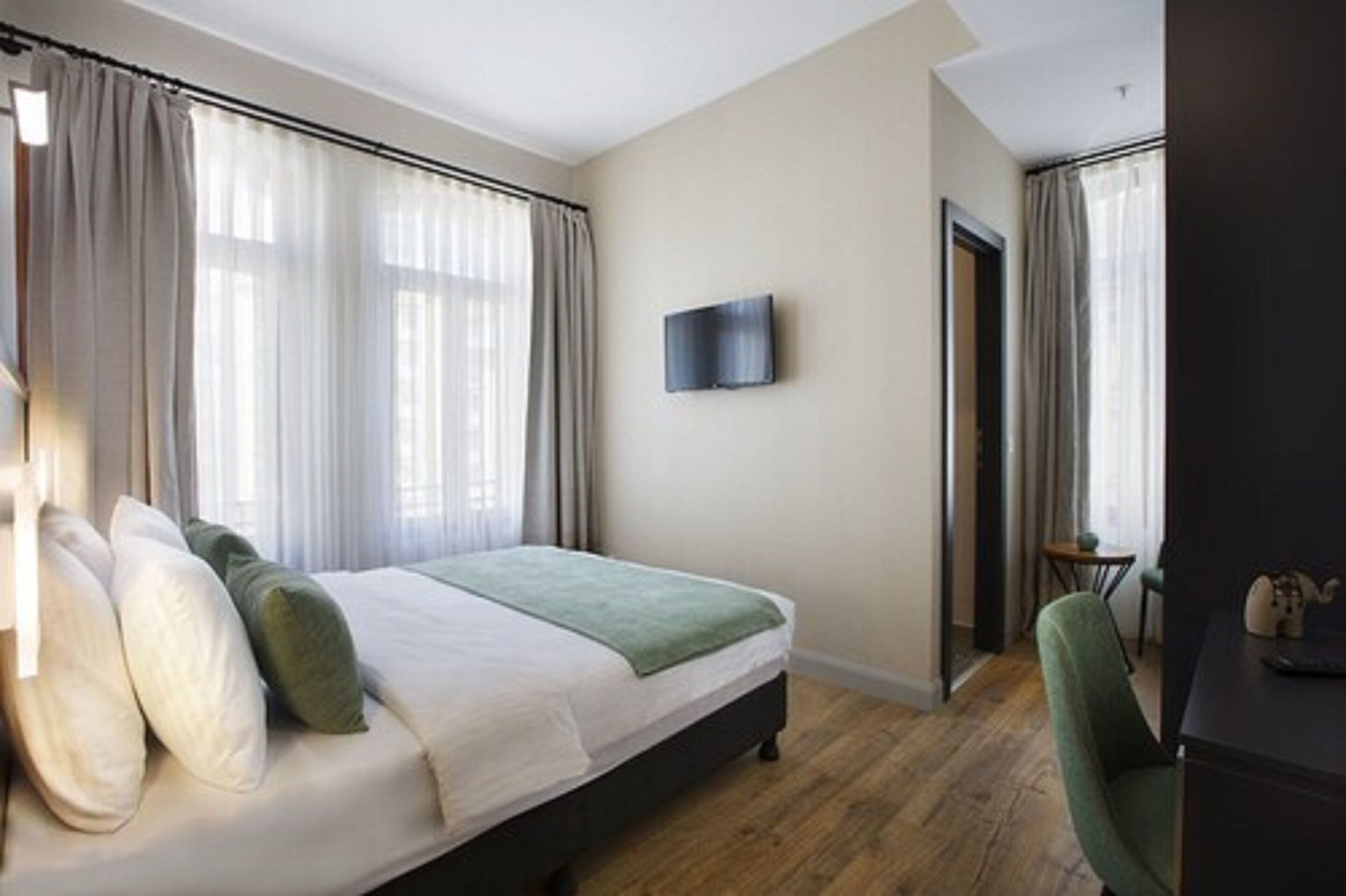 Habitación de hotel con cama, cortinas, televisor en la pared, escritorio y una silla.
