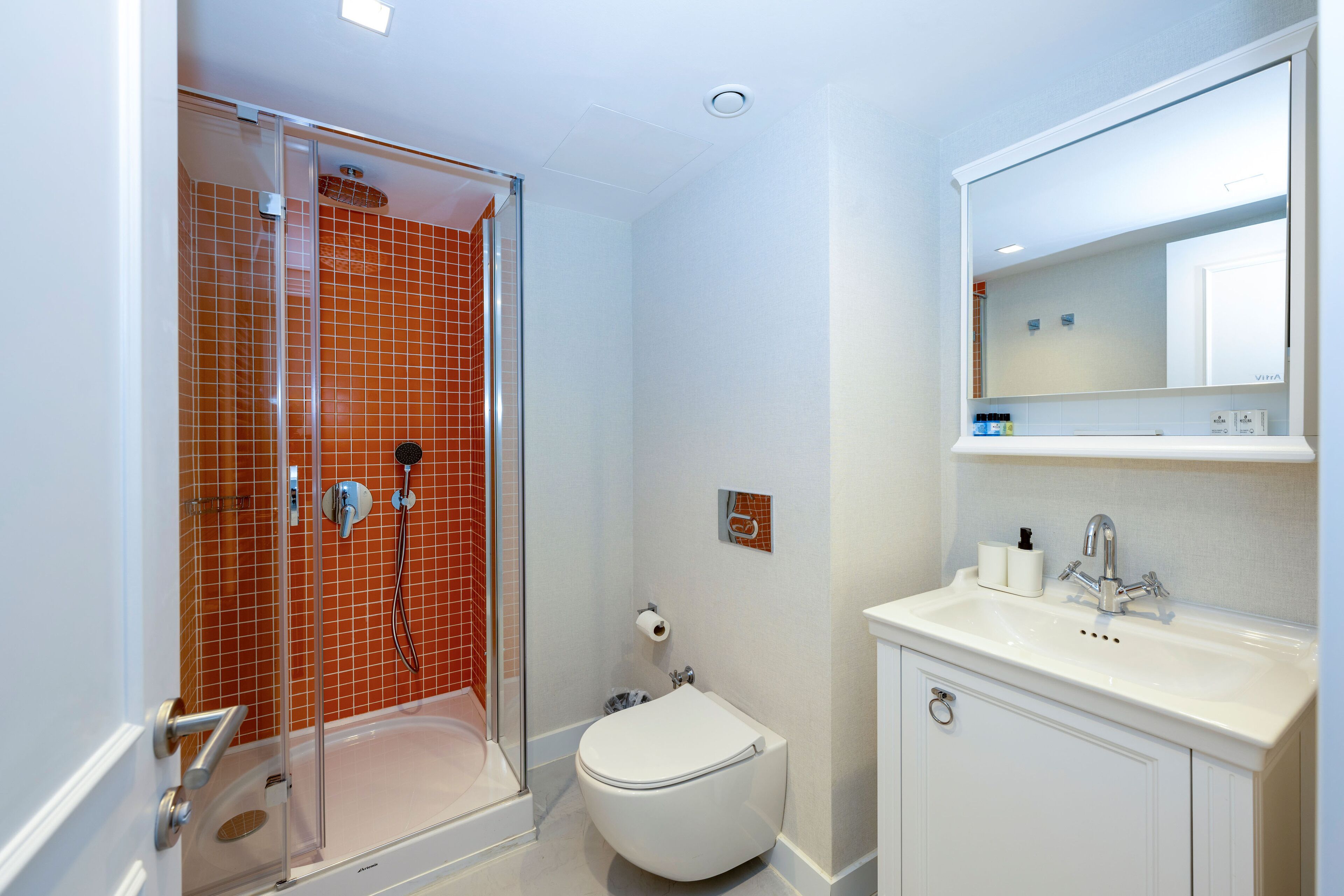 A modern bathroom with a glass-enclosed shower, a white toilet, and a white sink with a mirror above.