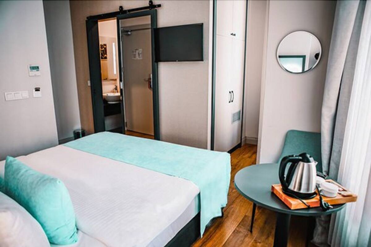 A hotel room with a bed, a small table with a kettle, and a mirror on the wall.
