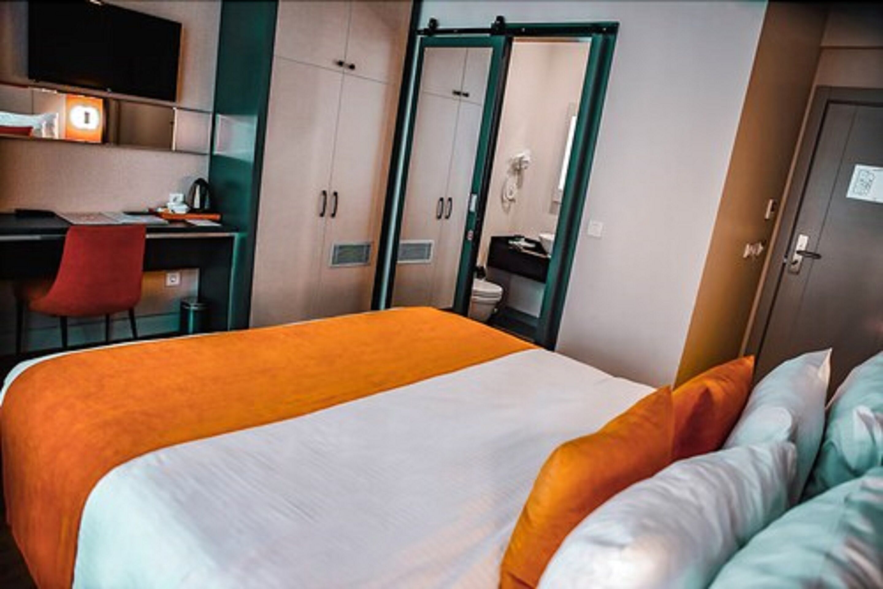 A hotel room with a bed, a desk, a chair, and a wardrobe.