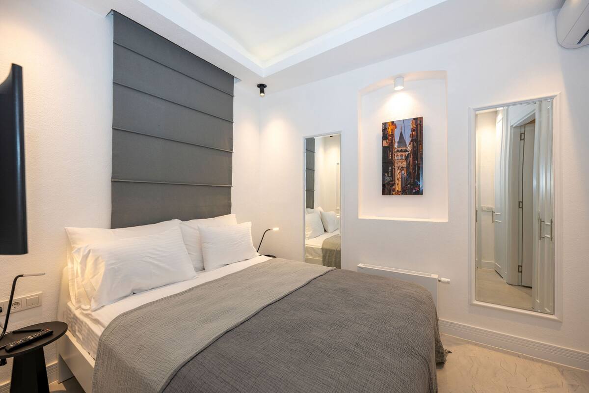 A modern bedroom with a large bed, bedside tables, a mirror, and a painting on the wall.