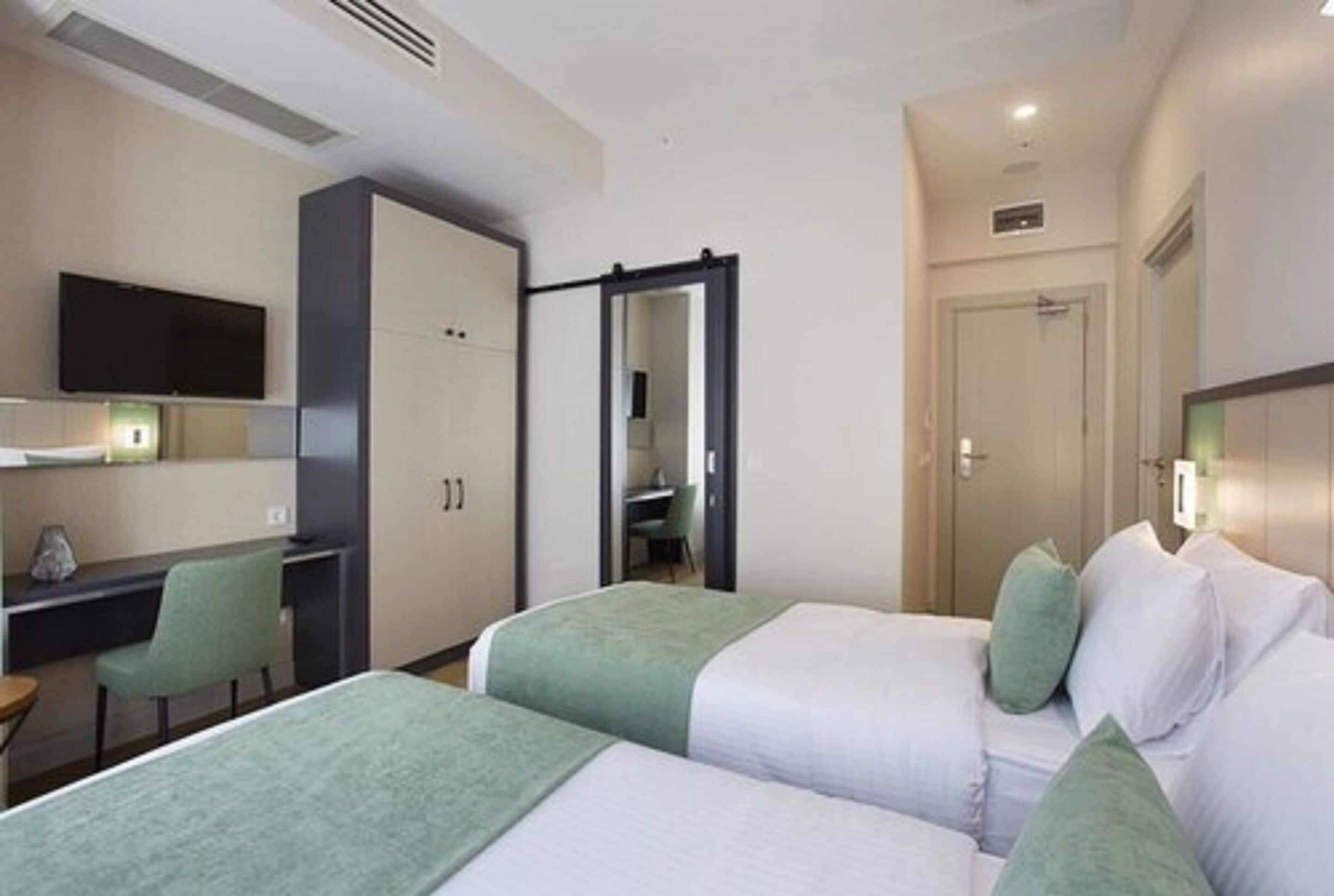 A hotel room with two beds, a desk, a chair, a TV, and a wardrobe.