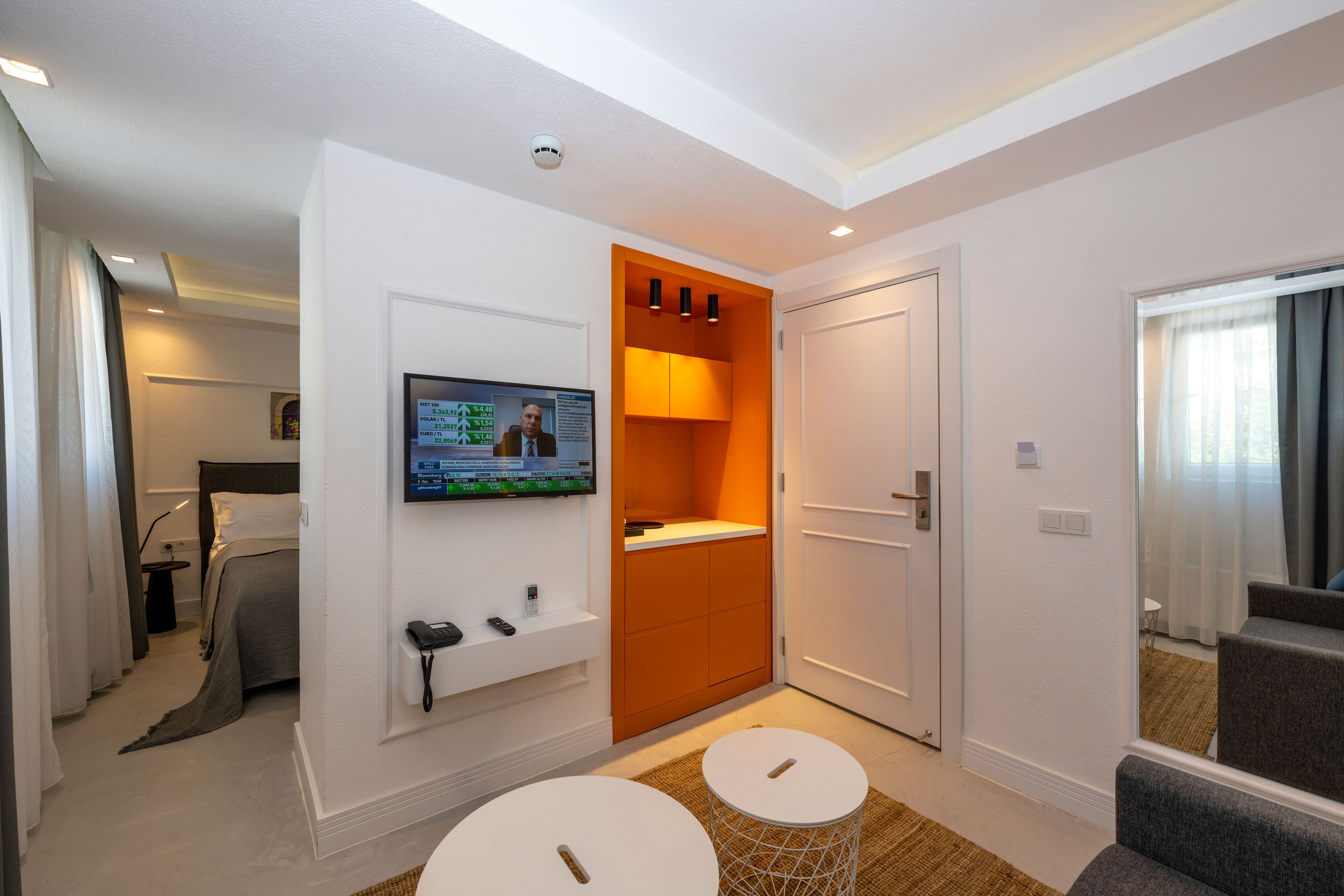A hotel room with a bed, a TV mounted on the wall, a small table, and a door leading to another room.