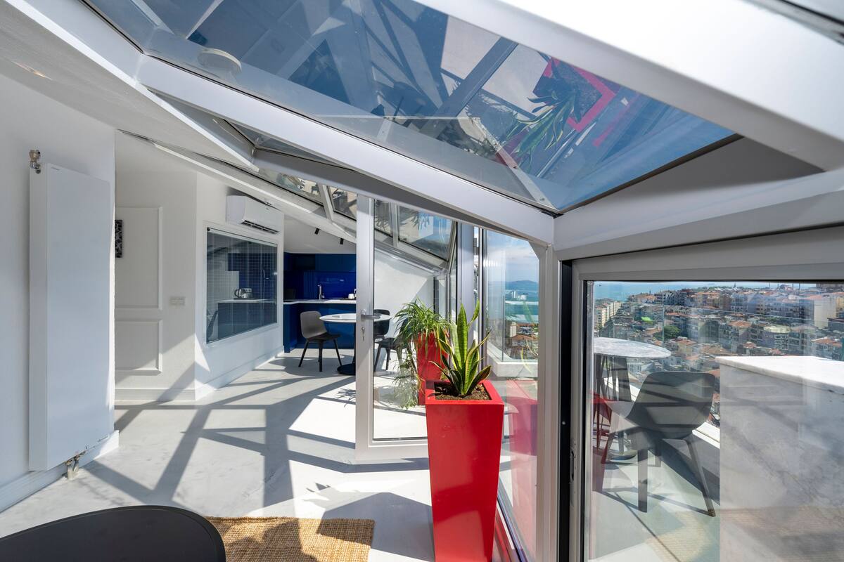 A modern apartment with a glass ceiling, a red planter, and a city view.