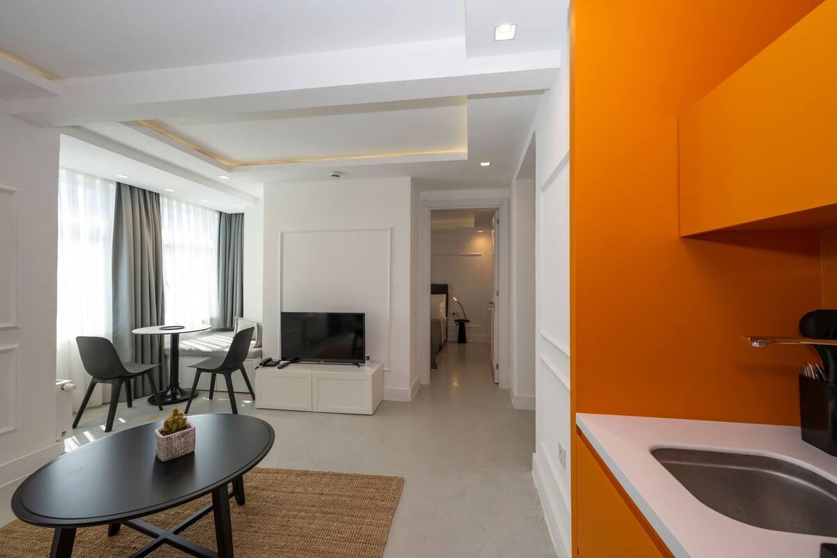 A modern living room with a dining area, a TV, and a kitchen with a sink.