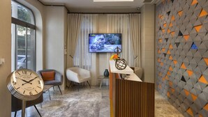 A modern reception area with a large TV screen, comfortable seating, a clock, and a decorative wall. - Juno Hotel Taksim (Istanbul)