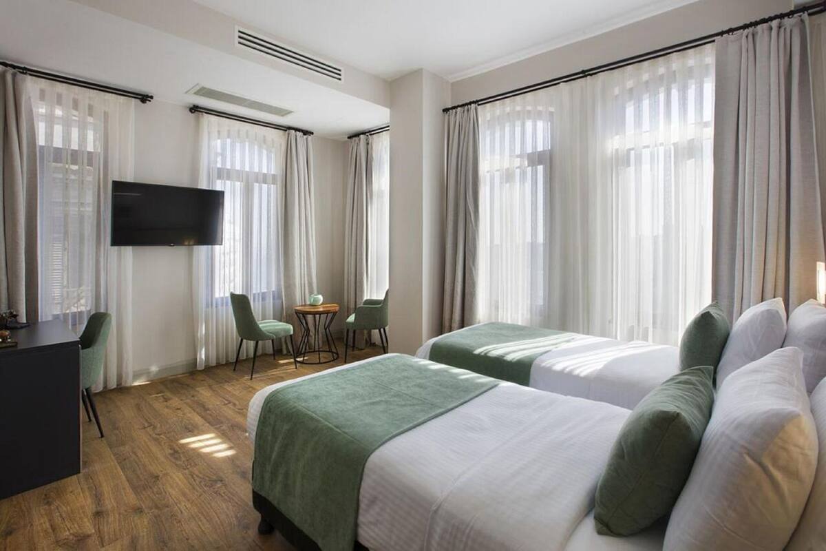A hotel room with two beds, a desk, a TV, and a small table with chairs.