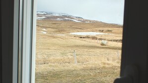 A view through a window of a grassy field with a fence and a distant hill. - Neðra-Vatnshorn (Hvammstangi)
