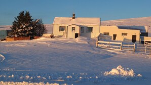 A snow-covered house with a wooden fence, a snow-covered tree, and a clear sky. - Neðra-Vatnshorn (Hvammstangi)