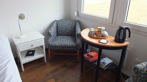 A small room with a bed, a desk, a chair, a table with a tray of items, and a window with a view of a field. - Neðra-Vatnshorn (Hvammstangi)